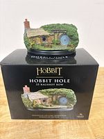 Front view of 35 Bagshot Row Hobbit Hole collectible displayed on its black base with 'Hobbit Hole 35 Bagshot Row' print, with the box underneath showing the same image.
