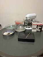 Wide shot of all items on table including mixer, attachments, bakeware and cookie cutters