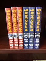 Six hardcover volumes shown from spine view: three red Golden Age Dailies and three blue Silver Age Dailies.