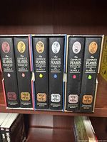Six hardcover Peanuts volumes from 1967 to 1978 with illustrated character badges on spine, on shelf.