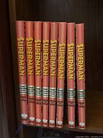 Nine red-spined hardcover volumes on shelf, spines show “Superman,” age labels and year ranges, IDW logo at base
