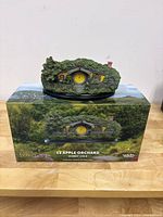 Front view of model on display base atop original box showing orchard scene artwork and title '13 Apple Orchard Hobbit Hole'.