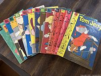 Photo of 13 Tom and Jerry comics fanned out on wood table, showing various colorful vintage covers with Dell Comics branding.