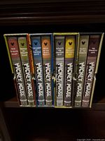 Eight spines lined up on shelf showing volume titles and color-coded bands.