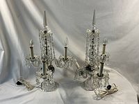 Pair of cut glass girandole lamps with three lights each, displayed against a white backdrop, showing both lamps side by side with cords attached.