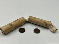 Two rolls of Indian Head Pennies with two loose pennies placed between them, showing condition and packaging.