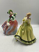 Front and side view of two Royal Doulton figurines in period dresses, showing color and details of clothing and posture.
