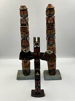Three vintage hand carved hand painted totem poles photographed frontally showing full poles and bases for size comparison.