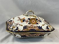 View of the lidded tureen sits on a flat surface showing intricate Imari Kings floral pattern and gold accents.