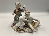 Front view of antique porcelain figurine showing two children, one holding an arm raised and the other reclining, plus a white bust sculpture.
