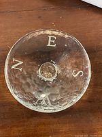 Top view of clear glass art bowl showing compass letters N, E, S, W on rim and textured surface.