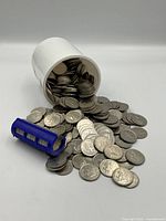 White plastic coin container tipped over, spilling coins; blue plastic quarter tube on left