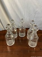 Six clear cut glass decanters with ribbed and starburst cut pattern shown on wooden surface with white background.