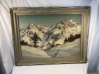 Framed oil painting showing full winter mountain landscape with snow and pine trees.