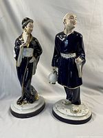 Pair of Asian-themed porcelain figurines, male and female, standing on oval bases with floral and gilt accents