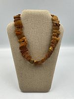 Front view of the amber choker necklace displayed on a beige fabric jewelry bust stand, showing the raw irregular amber resin pieces in shades of brown and yellow.