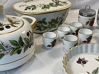 Close-up on large covered serving dish, teapot, egg cups and condiment jars showing detailed fruit motifs and gold edges.
