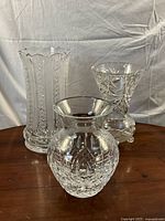 Three clear cut glass vases displayed together on wooden surface, showing overall shape and size differences