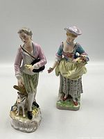 Front view of both porcelain figurines showing male with dog and bird and female with flowers.