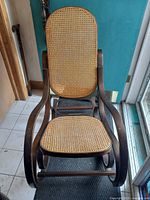 Front view of bentwood rocking chair showing rattan seat and backrest with curved wooden arms and legs.
