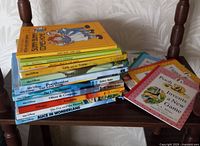 Stack of twenty children's books including Disney storybooks and Winnie the Pooh soft cover books shown on chair.