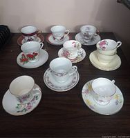 Full view of nine teacups with saucers showing various floral and anniversary designs