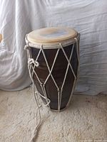 Full view of the barrel-shaped wooden dholak drum showing its dark brown wood body and white rope tensioning system