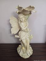 Front view of the cream resin fairy girl sitting and holding a large flower, showing delicate facial features and wings.