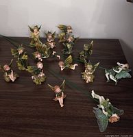 A spread of 14 green fairy tabletop ornaments and two plant picks arranged on a dark surface, showing various fairies in different poses and wing styles.