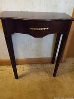 Front view of dark wood hallway/half table with brass accent on drawer front and tapered legs.