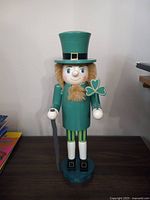 Front view of the Irish man wooden nutcracker showing detailed face, green top hat, coat, shamrock in hand, cane, and base.