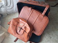 Three brown leather luggage pieces stacked together; large suitcase on bottom, medium suitcase and carry-on inside