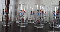 Eight clear glasses with colorful Nagano 1998 Winter Olympics logo and Olympic rings on each glass, arranged on a dark brown surface.
