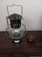 Large metal oil lantern with clear glass globe next to a small amber glass oil lantern missing its glass top, displayed on a dark wooden surface.