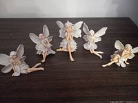 Five fairy ornaments in various seated and reclining poses on a dark wooden surface.