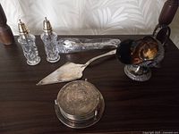 Full display of sterling silver and crystal silverware set including salt and pepper shakers, serving spatula, silver box, footed bowl, scoop, and wrapped silver utensil.