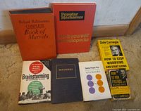 Seven vintage books arranged in two rows on a carpeted floor, showing titles and covers with some wear.