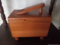 Angled view showing smooth wooden finish, ridged handle for lid, and rounded legs raising the box.