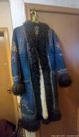 Full view of vintage suede and sheepskin coat hanging on hanger showing embroidery on sleeves and fur trimmed cuffs and hem.