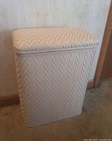 White wicker laundry hamper, rectangular shape with a lid closed, showing textured woven pattern.