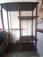 Front view of wooden shelves showing four tiers and turned spindle supports with a dark wood finish.