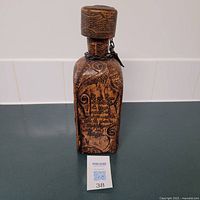 Front view of the antique leather wrapped cognac bottle showing engraved artwork and Spanish text on leather