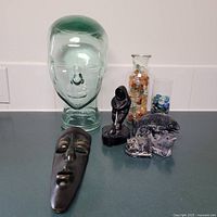 Full view of all art items, including glass head, face mask, seated figure, fish, bear and whale sculptures, and vases with marbles.