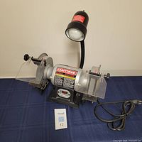 Front view of Craftsman bench grinder on table with attached lamp and power cord.