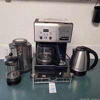 Full view of the coffee making appliances on a counter, showing the Cuisinart coffee maker, coffee grinder, French press, kettle, and pod holder.