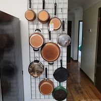 Pots and pans hanging on wall grid, showing copper-colored pans and cast iron pans