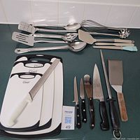 Full view of cutting boards, knives, sharpening steel, and hanging utensils spread on a surface