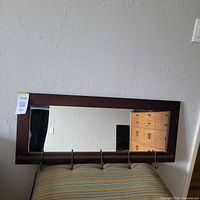 Front view of a rectangular mirror with dark wood frame and five metal hooks attached along the bottom.