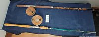 Wide shot of two vintage fishing rods with their reels on a dark blue cloth surface.