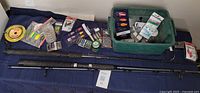Fishing rods laid out flat with green tackle tote and assorted fishing items on table